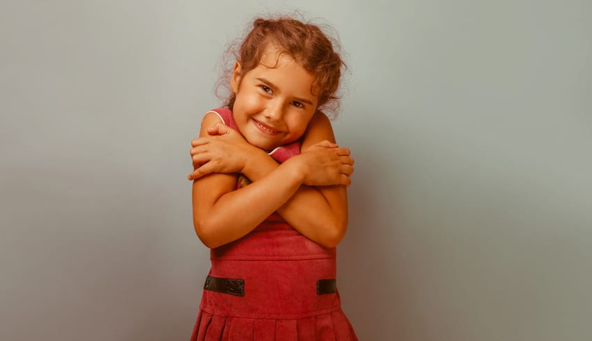 Girl European appearance decade hugging herself on a blue backg
